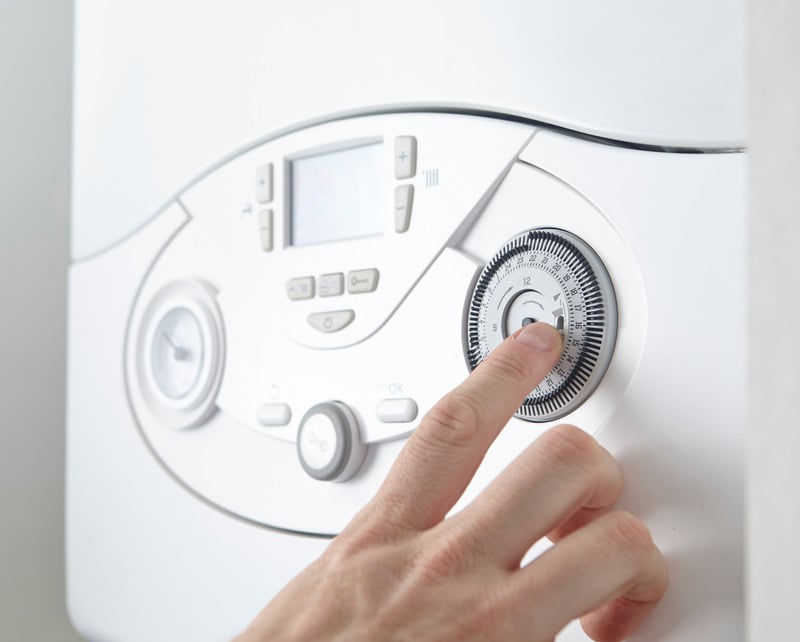 A hand adjusts the time dial on a white boiler with a digital display and control buttons. The scene suggests precise temperature control and modern technology.