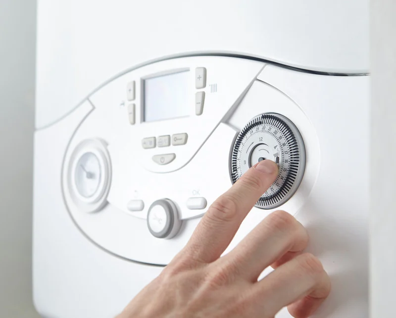 A hand adjusts the time dial on a white boiler with a digital display and control buttons. The scene suggests precise temperature control and modern technology.
